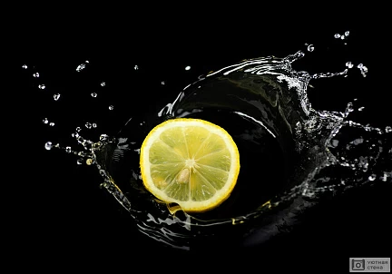 Желтый лимон в брызгах воды на черном фоне